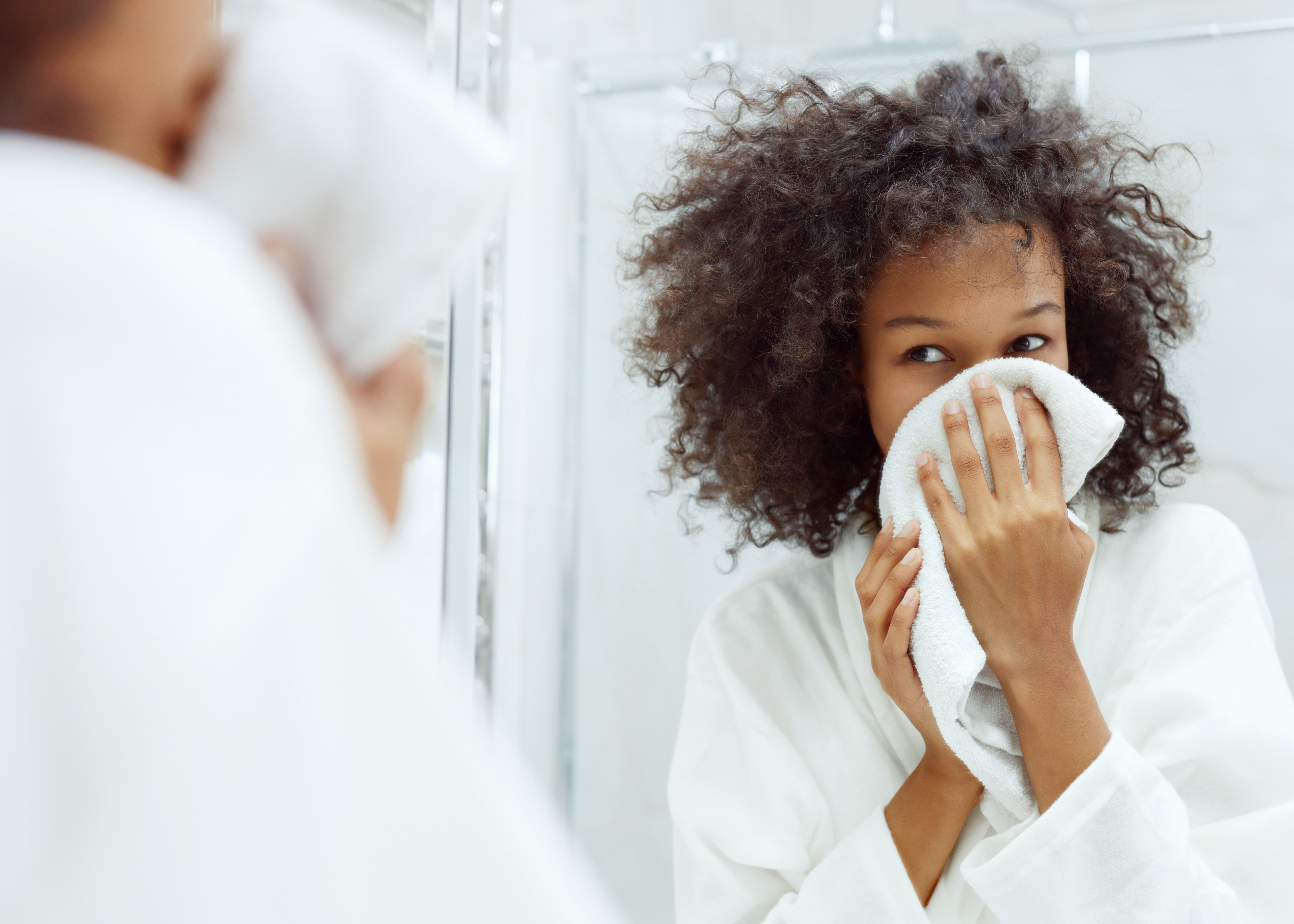 Attractive black woman in mirror patting face with towel  skincare